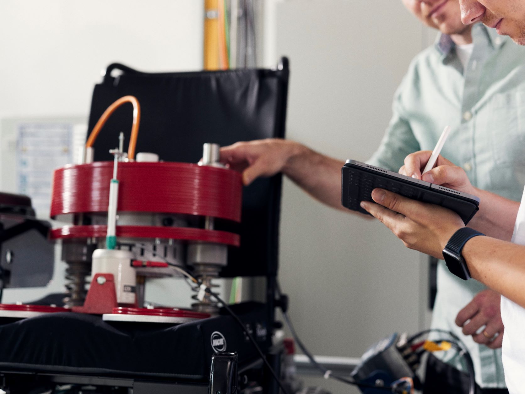 Zwei Personen schauen auf ein Tablet und arbeiten mit einem technischen Rollstuhl