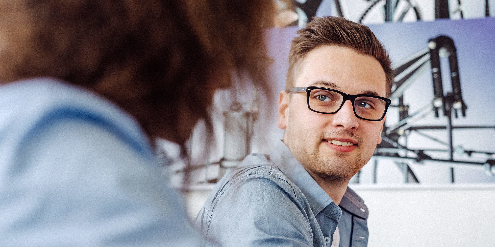 Eine Person mit Brille unterhält sich mit einer anderen Person.