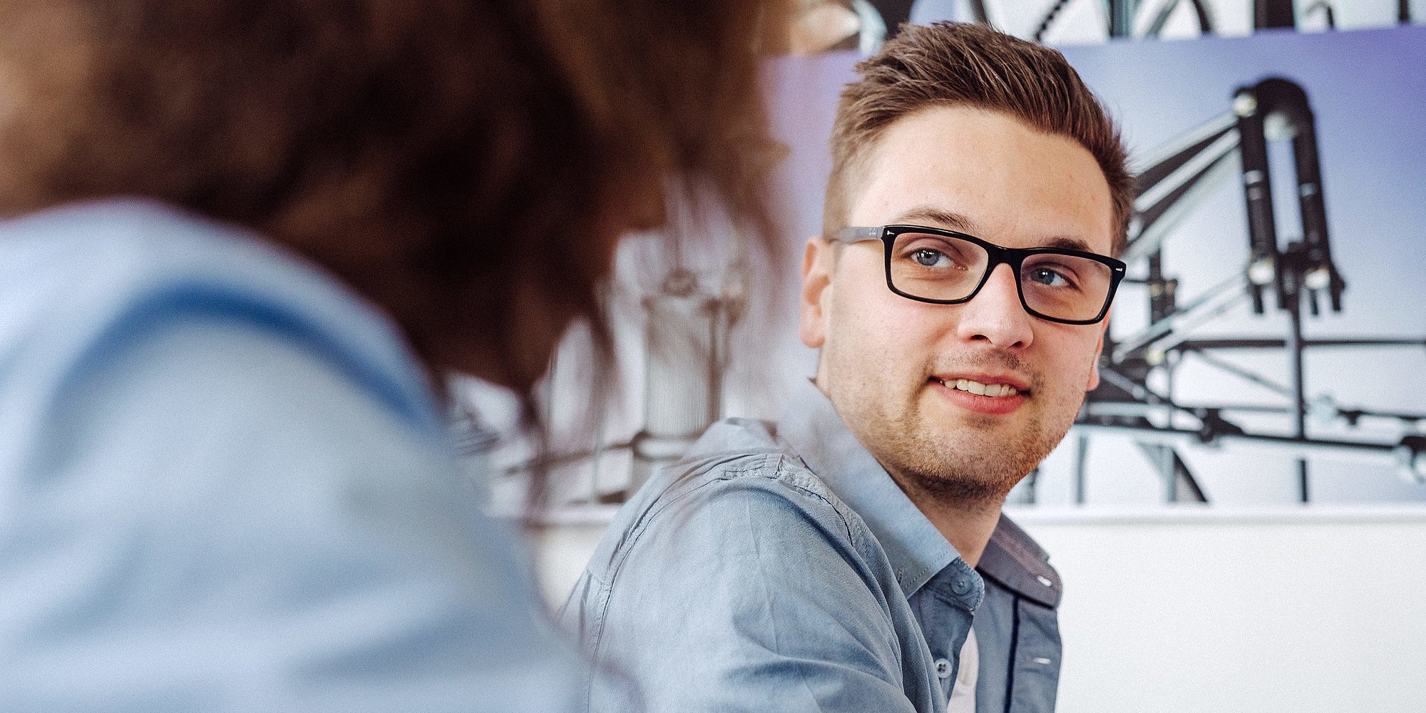 Eine Person mit Brille unterhält sich mit einer anderen Person.